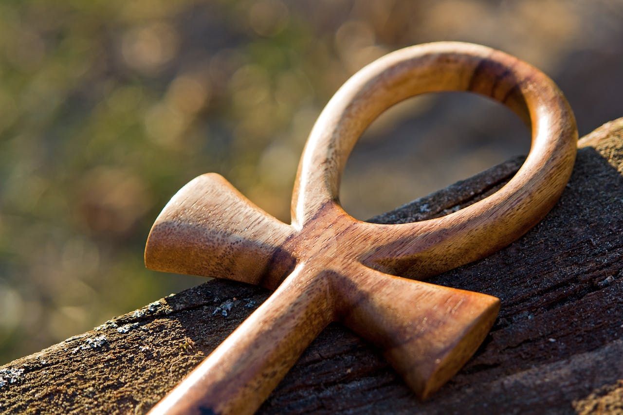 Detailed view of a wooden ankh symbol resting on a tree trunk, emphasizing its spiritual and historical significance.