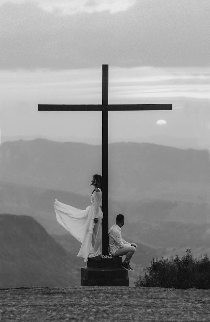 A serene moment of spiritual reflection by a cross at sunset with a dramatic sky in the background.